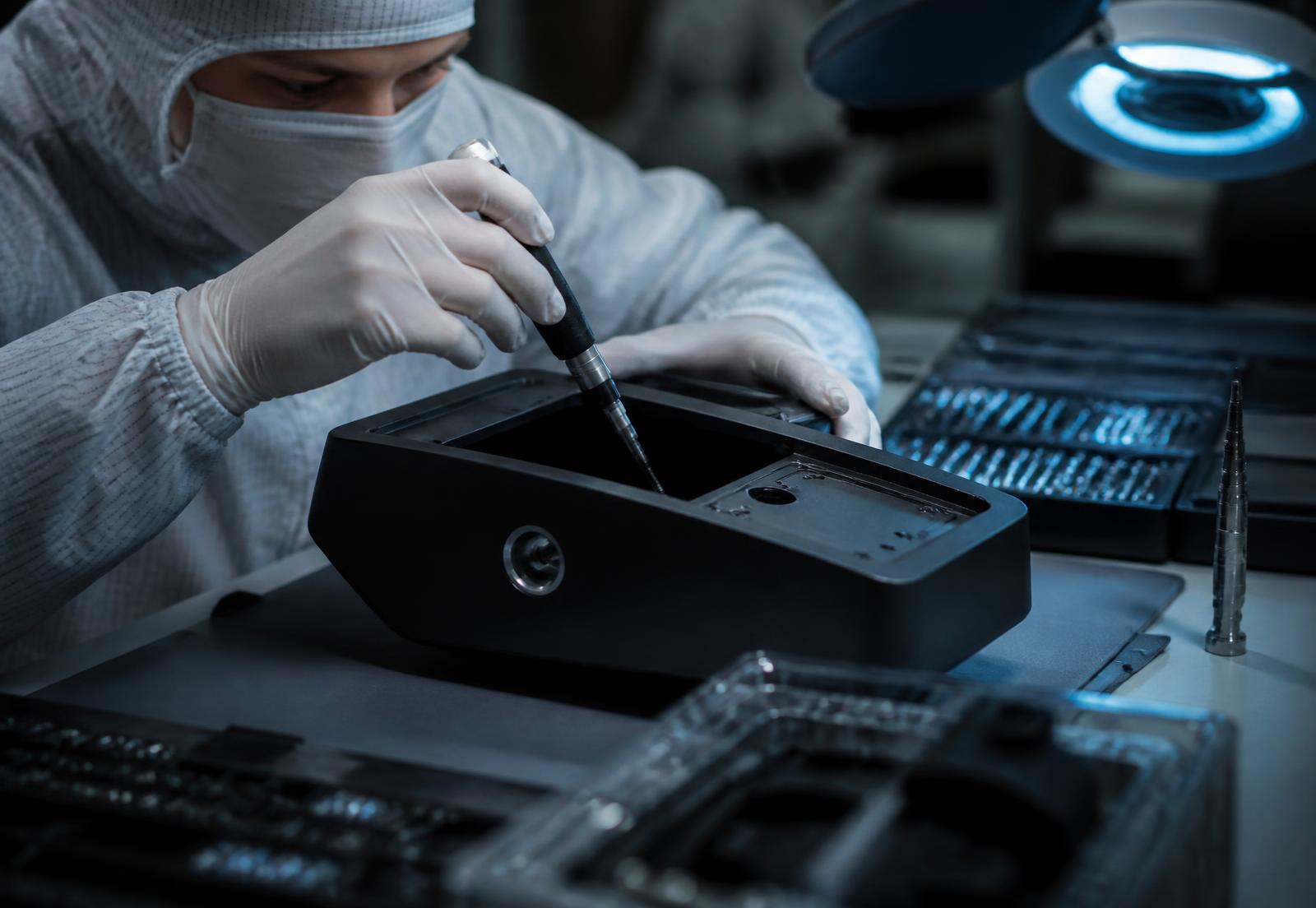 Technician assembling a matte black medical device enclosure in a cleanroom