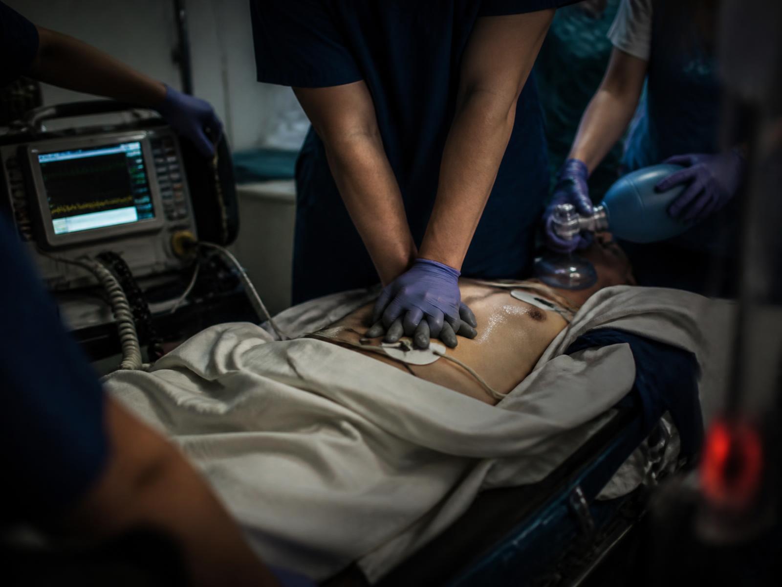Resuscitation team performing chest compressions beside a cardiac monitor