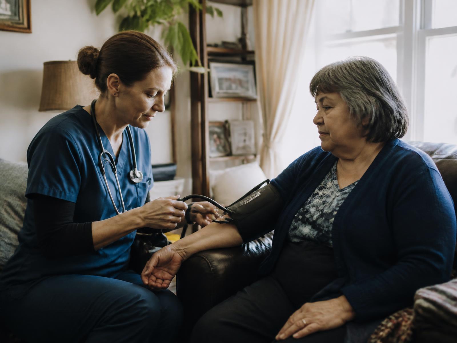 Home-health nurse checking an older patient's blood pressure at home